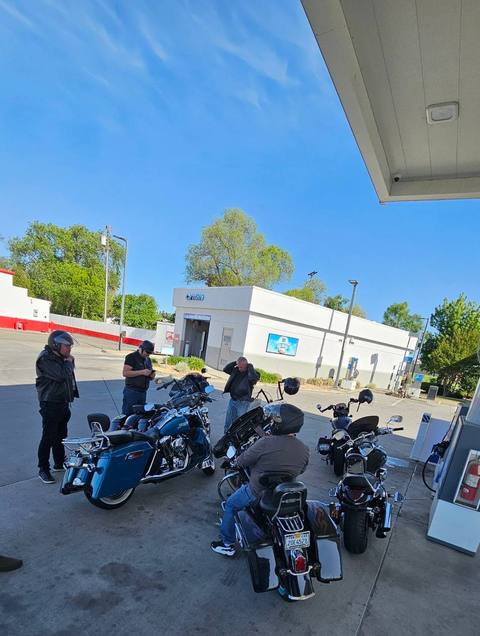 Riders with motorcycles beneath a fuel-station canopy.