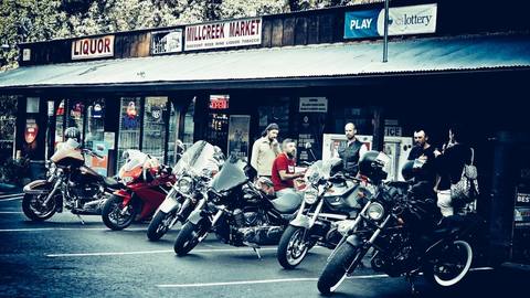 Riders and motorcycles outside a row of storefronts.