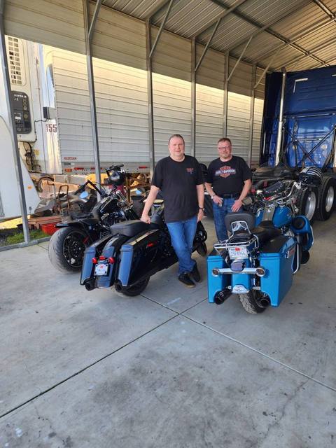 Two people standing beside motorcycles inside a garage.