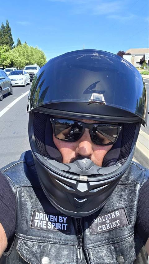 A close-up portrait of a rider wearing a motorcycle helmet and sunglasses.