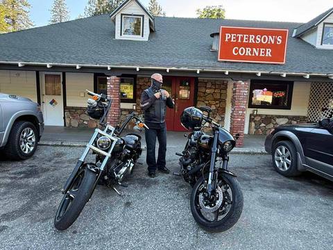 A rider standing beside two motorcycles outside a café.