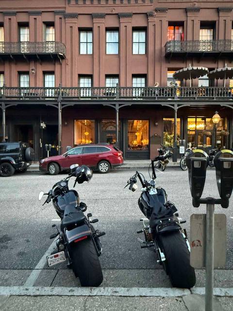 Two motorcycles parked across from a multistory brick building.